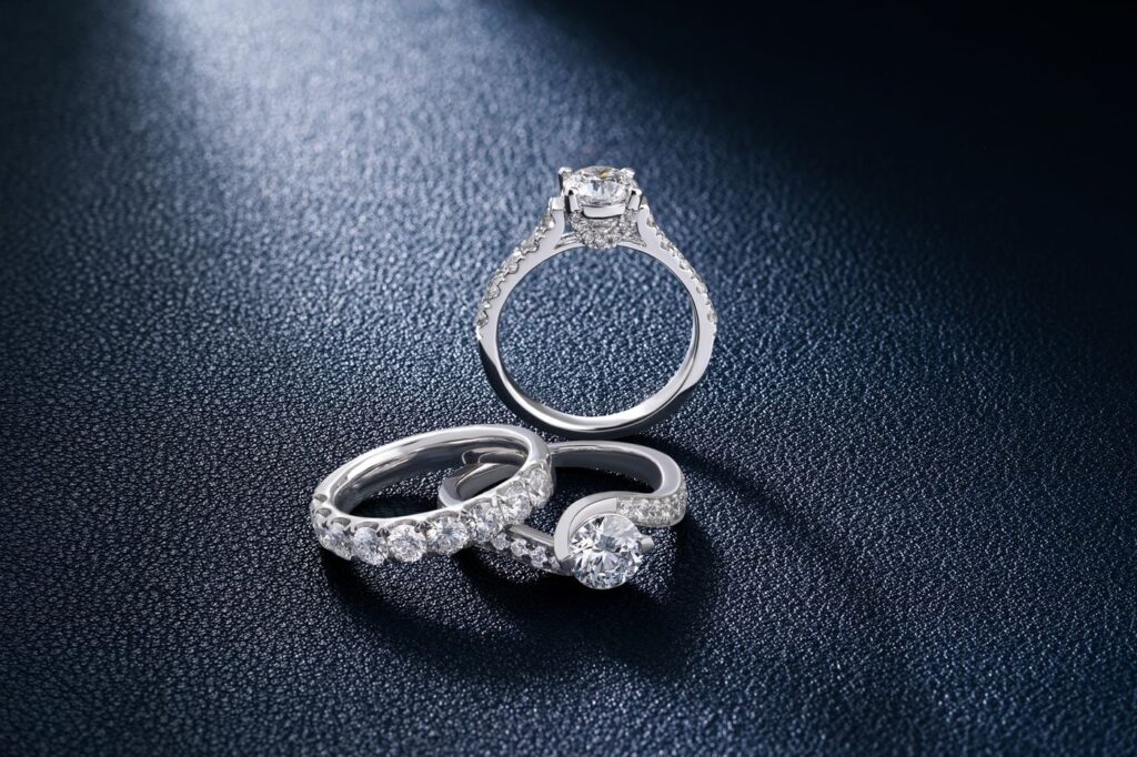 Three diamond engagement and wedding rings on a dark blue textured surface